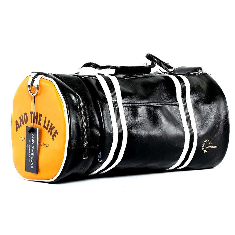 A black cylindrical duffel bag with white dual straps running vertically along the sides. The end panel of the bag is bright yellow with the words “AND THE LIKE” printed in bold letters. A small black tag also hangs from a metal ring on the side. The bag has a glossy leather-like finish and features zippered compartments.
